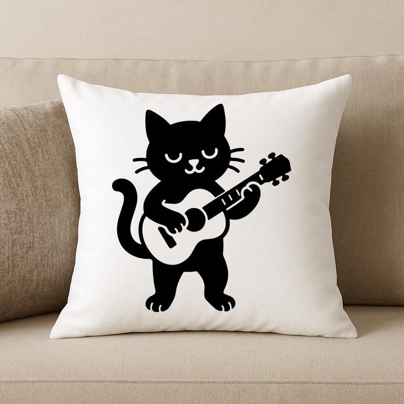 May include: White throw pillow featuring a black cartoon cat playing a guitar. The cat has a smiling face and is holding the guitar with both paws. The pillow is square and sits on a beige sofa.