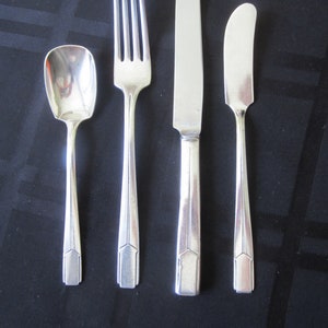 May include: A set of four silver-plated flatware pieces, including a fork, knife, butter knife, and a spoon. The pieces have a simple, elegant design with a geometric pattern.