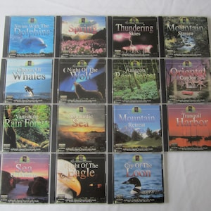 May include: A collection of 15 compact discs featuring nature sounds. The discs are arranged in three rows of five. The titles of the discs include "Swim With The Dolphins", "Spring", "Thundering Skies", "Mountain Stream", "Chorus Of Whales", "Night Of The Wolf", "Amazon Rain Forest", "Oriental Garden", "Vanishing Rain Forest", "Romantic Sea", "Mountain Retreat", "Tranquil Harbor", "Sea Of Dreams", "Flight Of The Eagle", and "Cry Of The Loon".