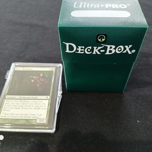 May include: A green Ultra-Pro Deck Box with the text "Ultra-Pro" and "Deck-Box" on the front. A clear plastic card holder with a Magic: The Gathering card inside is in front of the box.