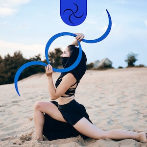 Peut inclure: Une personne portant un haut à capuche noir et un short noir pose avec des cerceaux bleus dans un décor désertique.