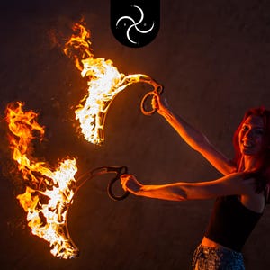 Könnte beinhalten: Eine Frau mit roten Haaren hält zwei brennende Poi, eine Art Feuer-Tanz-Requisite. Die Poi bestehen aus einer langen Kette mit einer gewichteten Kugel am Ende. Die Frau lächelt und schaut in die Kamera.