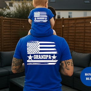 Puede incluir: Camisetas azul real con un dise&ntilde;o de bandera estadounidense desgastada. La camiseta del adulto dice "GRANDPA" y la del ni&ntilde;o "GRANDSON". El dise&ntilde;o incluye estrellas y rayas blancas.