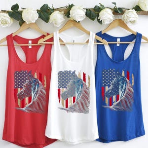 May include: Three racerback tank tops featuring an American flag and a horse's head design. The tank tops are red, white, and blue.