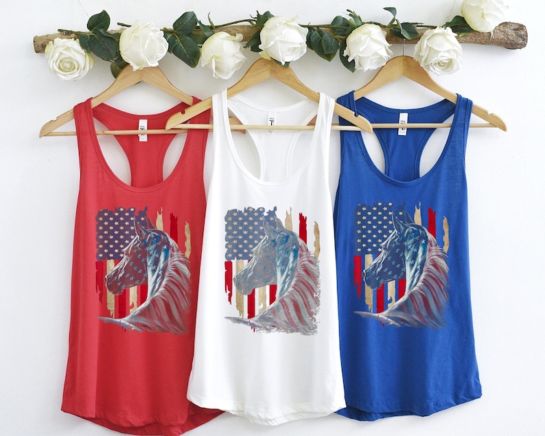 May include: Three racerback tank tops featuring an American flag and a horse's head design. The tank tops are red, white, and blue.