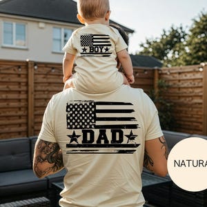 Puede incluir: Camisetas beige a juego con un dise&ntilde;o de bandera americana desgastada. La camiseta del adulto dice "DAD" y la del ni&ntilde;o "BOY". Las camisetas son de color beige claro.