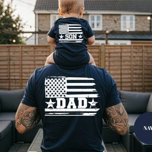 Puede incluir: Camisetas a juego de color azul marino con un dise&ntilde;o de bandera americana desgastada. La camiseta de la espalda dice "DAD" y la camiseta m&aacute;s peque&ntilde;a dice "SON". Las camisetas son un conjunto a juego.
