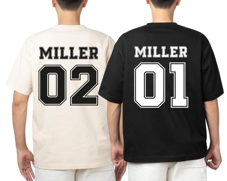 May include: Two short-sleeved t-shirts, one cream and one black, with the name "MILLER" and the numbers "02" and "01" printed on the back in a collegiate style. The numbers are outlined in a contrasting color.