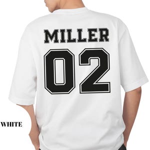 May include: White t-shirt with the name "MILLER" and the number "02" in black block letters. The shirt has a classic crew neck and short sleeves. The word "WHITE" is printed at the bottom left.