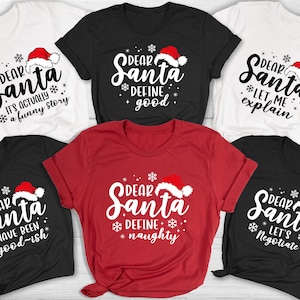 May include: A collection of Christmas-themed t-shirts in white, black, and red. Each shirt features the phrase "Dear Santa" with a Santa hat and a unique message, such as "It's actually a funny story" or "Define naughty."