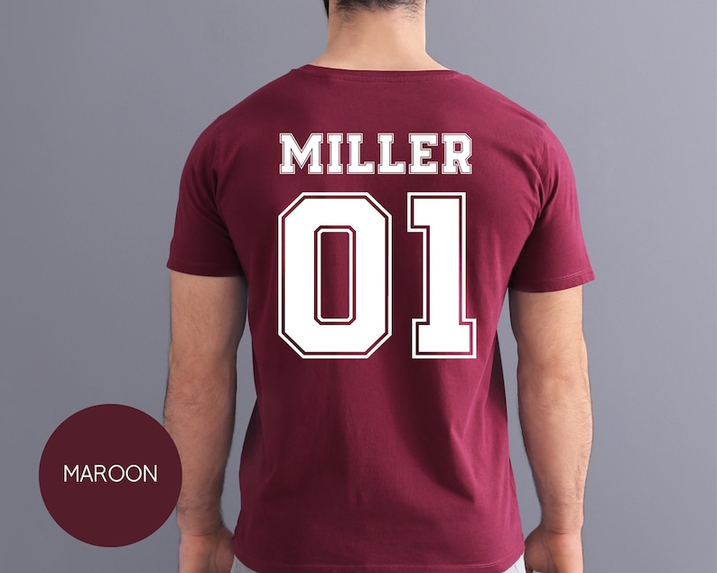 May include: Maroon t-shirt with the name "MILLER" and the number "01" in white, outlined lettering on the back. The shirt is a solid maroon color, and the text is in a bold, collegiate style font. The word "MAROON" is in a maroon circle.