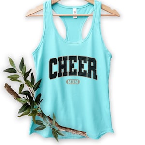 May include: A turquoise tank top with the text "CHEER MOM" in black letters with a gold outline.