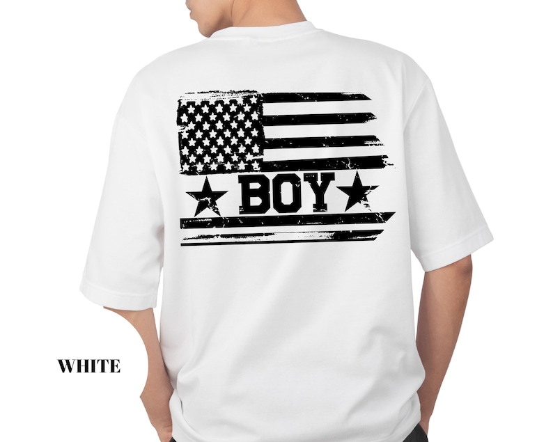 Puede incluir: Camiseta blanca con un dise&ntilde;o de bandera americana desgastada en la espalda. El gr&aacute;fico de la bandera incluye estrellas, rayas y la palabra "BOY" en negrita, con estrellas a cada lado. La palabra "WHITE" est&aacute; impresa en la parte inferior.