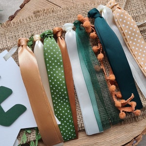 May include: A green felt letter E banner with a white background and a string of green, brown, and white ribbon with white polka dots and orange pom-poms.