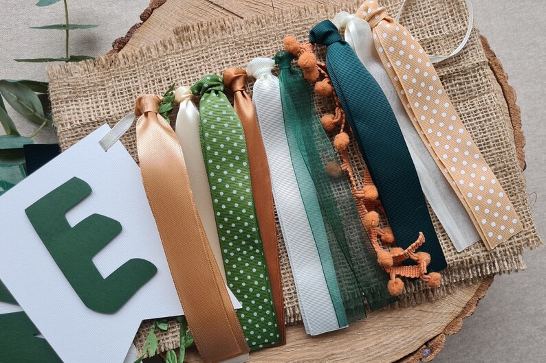 May include: A green felt letter E banner with a white background and a string of green, brown, and white ribbon with white polka dots and orange pom-poms.
