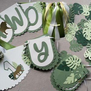 May include: Green and white paper banner with the words "Two-y" and a lion illustration. The banner is decorated with green paper leaves and green and white ribbon.
