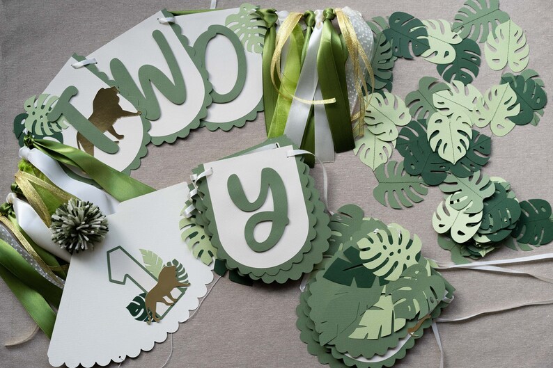 May include: Green and white paper banner with the words "Two-y" and a lion illustration. The banner is decorated with green paper leaves and green and white ribbon.