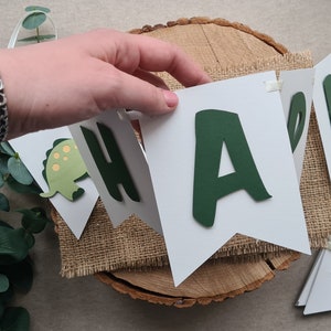 May include: A white banner with green letters spelling "Happy" with a green dinosaur cutout on one of the flags.