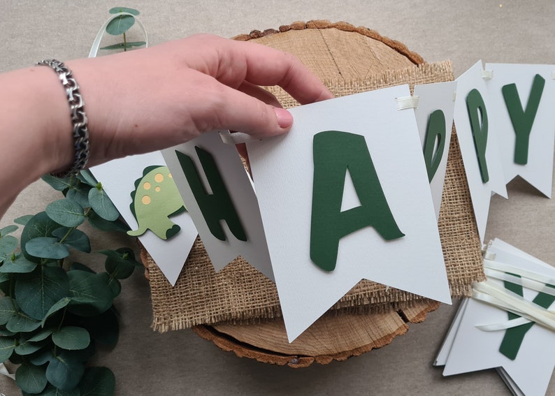 May include: A white banner with green letters spelling "Happy" with a green dinosaur cutout on one of the flags.
