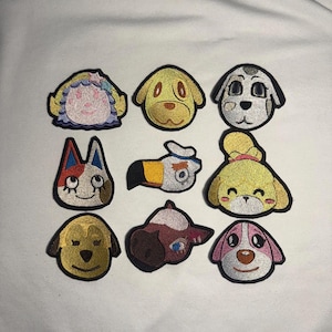 May include: Nine embroidered patches featuring various cartoon dog and cat characters. The patches are in various colors, including yellow, white, pink, and blue, with black outlines. The patches are likely for clothing or accessories.