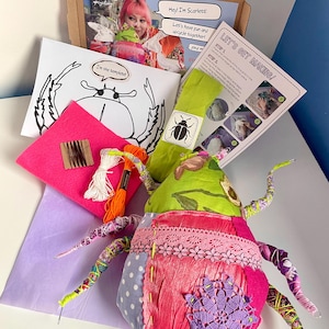 Könnte beinhalten: Ein Bastelset mit einem handgefertigten Stoffkäfer, einer Käferzeichnung und Anleitungen. Der Käfer besteht aus rosa, grünen und lila Stoffen mit Spitze und Stickereien. Das Set enthält Stickgarn und Filz.
