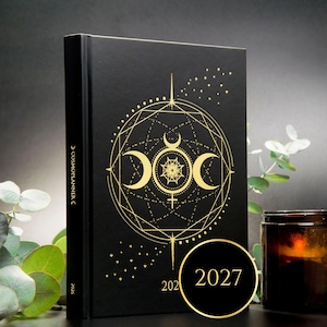 May include: A black hardback planner titled Cosmoplanner on the spine, featuring a gold foil celestial design of a triple moon and geometric patterns on the front cover. The year 2027 is printed in gold on the lower right corner of the cover.
