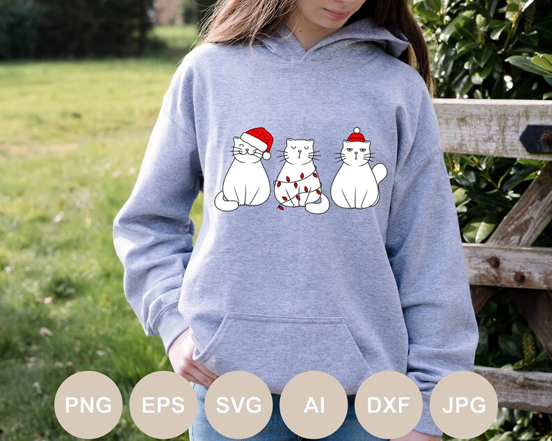 May include: A gray hoodie with a graphic of three white cats wearing Santa hats. The cats are in a row, with the middle cat wrapped in Christmas lights.