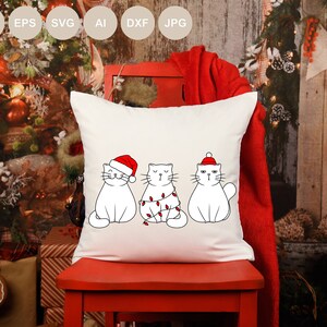 May include: White throw pillow with three white cats wearing Santa hats and Christmas lights. The cats are in a row, with the cat on the left wearing a Santa hat, the cat in the middle wearing Christmas lights, and the cat on the right wearing a Santa hat.