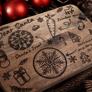 May include: Wooden Christmas serving board with engraved holiday designs. Features text "Dear Santa", "Santa's Treat", and "Reindeer snack". Includes images of a carrot, snowflake, snowman, gift, and Christmas tree. The board also has the text "Have a drink before you go, Merry Christmas Ho Ho Ho!"