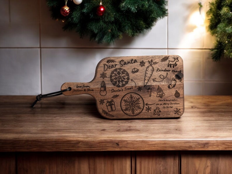 May include: A wooden cutting board with a handle, engraved with Christmas-themed illustrations and the words "Dear Santa." Includes a snowflake, snowman, carrot, reindeer, and gift box. A black cord is attached to the handle.