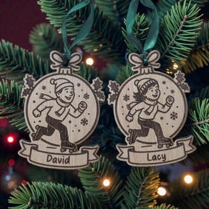 May include: Two wooden Christmas tree ornaments with a running skater design. Each ornament features a skater wearing a hat and scarf, with the names "David" and "Lacy" on a banner. The ornaments are suspended by green ribbons.