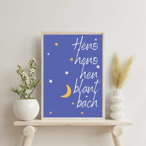 Puede incluir: Una impresión enmarcada con un fondo azul presenta escritura blanca e ilustraciones de estrellas y una luna creciente. El texto dice "Heno heno hen blant bach". El marco es de color madera clara.
