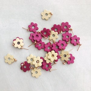 May include: A collection of pink and cream flower-shaped earrings with gold accents. The earrings are arranged in a cluster on a white surface.