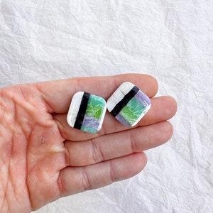 Op de afbeelding: Een paar vierkante oorbellen met een marmerpatroon in wit, zwart, groen en paars.