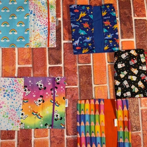 May include: Six different book covers with various colourful patterns. The covers feature designs of rainbows, stars, dinosaurs, cats, and pencils.