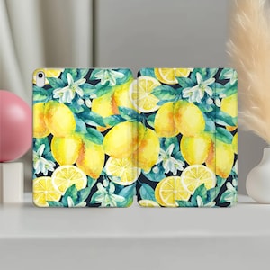 Puede incluir: Una funda de tableta abierta con un diseño de acuarela de limones, hojas y flores blancas sobre un fondo oscuro. La funda está diseñada para proteger la tableta y añadir un toque de estilo. La funda está abierta, mostrando el diseño interior.