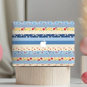 May include: Laptop skin featuring a patchwork design with various floral and geometric patterns. The design incorporates stripes of blue gingham, polka dots, and floral prints in red, yellow, and blue. The Apple logo is visible.