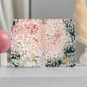 May include: A tablet case with a floral design in shades of pink, white, green, and gold. The case is open, revealing the tablet screen and a stylus. The design has a textured, dotted appearance.