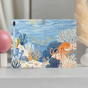 Könnte beinhalten: Tablethülle mit einem Unterwasser-Aquarelldesign. Die offene Hülle zeigt einen blauen Hintergrund mit Korallen, Fischen und einem orangefarbenen Oktopus. Ein Stift ist links sichtbar. Die Hülle schützt das Tablet.