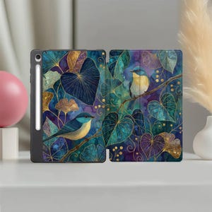 May include: A tablet case featuring a dark blue and purple watercolour background with gold-lined ginkgo leaves and two small blue birds perched on branches. The case includes a dedicated slot for a stylus pen on the left side edge.