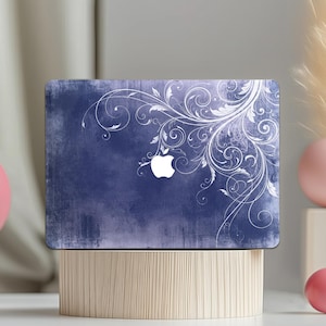 Op de afbeelding: Een laptophoesje met een verweerde marineblauwe achtergrond en een wit bloemmotief. Het Apple-logo is zichtbaar. De hoes wordt gepresenteerd op een houten standaard.