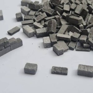 Peut inclure: Une collection de petits morceaux de pierre rectangulaires gris, dont certains sont disposés pour ressembler à un mur miniature. Les pièces varient légèrement en taille et en forme, avec des surfaces rugueuses et texturées. L'image montre un tas de ces morceaux de pierre.