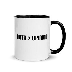 Könnte beinhalten: Weiße Keramik-Kaffeetasse mit schwarzem Rand und Henkel. Die Tasse hat den Text "DATA > OPINION" in Schwarz auf der Vorderseite aufgedruckt.