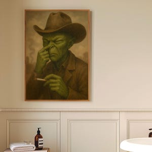 Könnte beinhalten: Ein gerahmtes Gemälde einer grünhäutigen Figur mit Cowboyhut, die eine Zigarette hält, hängt an einer weißen Wand. Ein kleiner Holzschemel mit Handtuch, Seife und einer Flasche steht unter dem Gemälde. Das Badezimmer hat einen schwarz-weiß karierten Boden.