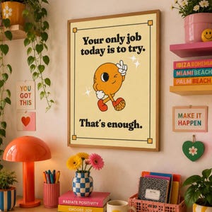 May include: A rectangular wall poster with a light yellow background and a black border. The text reads: Your only job today is to try. That's enough. In the center is a cartoon orange circular character with a face, arms, and legs.