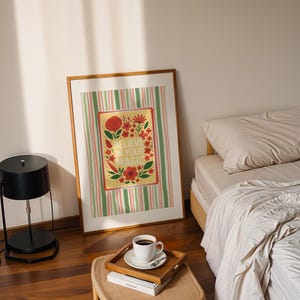 May include: A framed rectangular wall art print featuring a yellow center panel with red and orange flowers, green leaves, and the text BELIEVE IN YOUR MAGIC, surrounded by a background of vertical green, pink, and white stripes in a wooden frame.