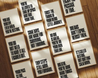 May include: A collection of framed art prints with motivational quotes in black text on a white background. The prints are arranged on a wooden surface, with various phrases like "You are worthy" and "Dreams don't expire."
