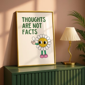 以下が含まれることがあります： 緑色の「THOUGHTS ARE NOT FACTS」というテキストが入ったフレーム入りプリント。プリントには、黄色の中心、白い花びら、緑色の茎、ピンクの靴を持つ漫画のデイジーが描かれています。フレームは金色です。