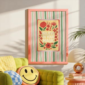 May include: A framed wall art print featuring a yellow rectangular center with red flowers and green leaves surrounding the text BELIEVE IN YOUR MAGIC. The background of the print has vertical stripes in shades of green, pink, and white.