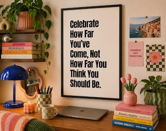 May include: A framed wall art print featuring the black text: Celebrate How Far You've Come, Not How Far You Think You Should Be. The print is displayed in a thin black frame, showcasing a motivational quote in a bold, sans-serif typeface.